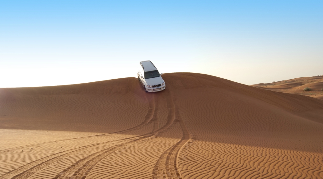 4X4 suv driving downwards from the top of the desert dune during sunset